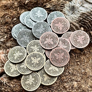May include: A collection of round, metal tokens with a fairy design. The tokens are in various shades of silver, gold, and copper. Each token features a fairy with wings and the text "A Gift From Your Tooth Fairy".