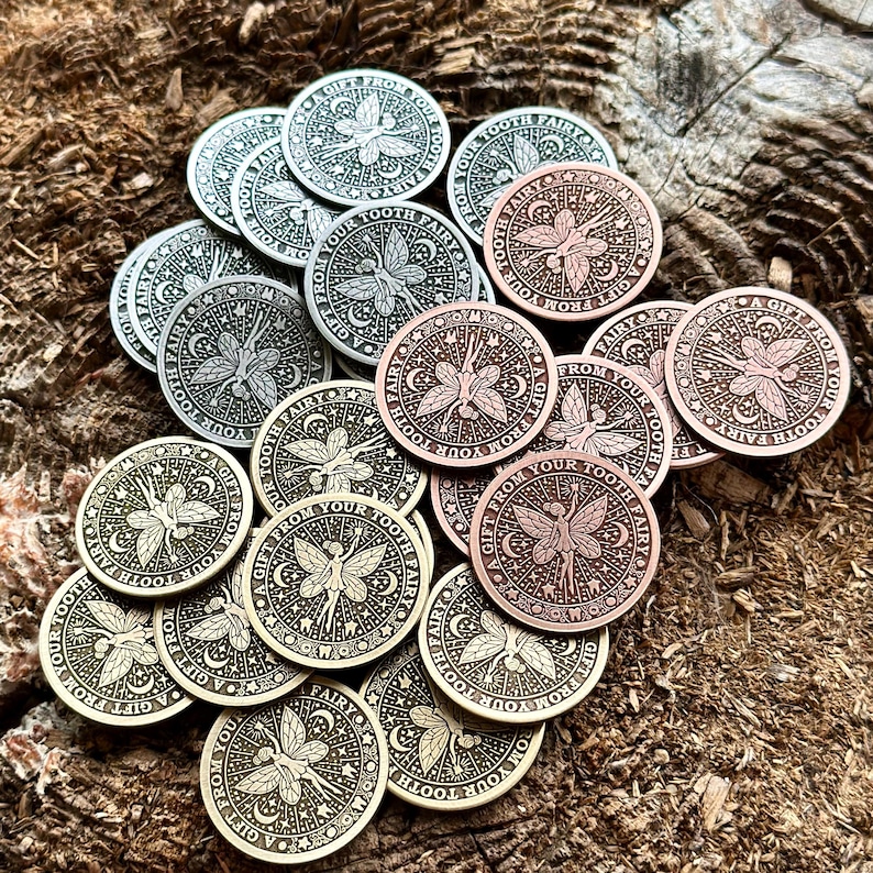 May include: A collection of round, metal tokens with a fairy design. The tokens are in various shades of silver, gold, and copper. Each token features a fairy with wings and the text "A Gift From Your Tooth Fairy".