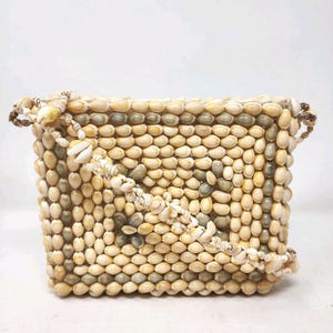 May include: A small, rectangular handbag made entirely of beige and brown seashells. The bag has a shoulder strap made of the same shells.