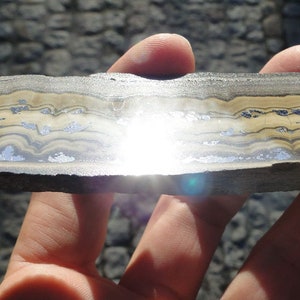 May include: A close-up of a banded rock with alternating layers of light brown and dark gray. The rock is smooth and polished, and the layers are clearly visible.