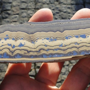 May include: A close-up of a banded rock with alternating layers of brown, white, and blue. The rock has a smooth, polished surface.
