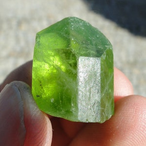 May include: A large, green, faceted crystal with a silvery sheen. The crystal is translucent and has a slightly irregular shape.