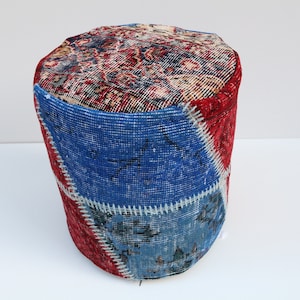 May include: A round, blue and red patchwork ottoman made from repurposed rugs. The ottoman is covered in a variety of patterns and colours, including blue, red, and white.