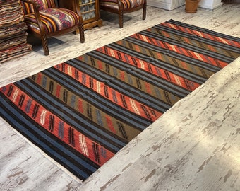 May include: A traditional handwoven rug with a striped pattern in shades of blue, red, brown, and beige. The rug is laid out on a light wood floor.