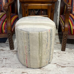 May include: A round, white and beige patterned ottoman with a striped design. The ottoman is made of woven fabric and has a slightly textured surface.