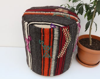 May include: A round, woven ottoman with a colorful striped pattern in shades of red, orange, white, and black. The ottoman is made of wool and has a traditional design.