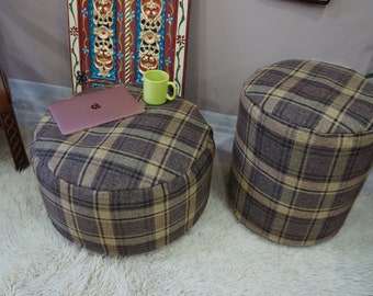 May include: Two brown and beige plaid round ottomans with a laptop and a green mug on top of one of them.