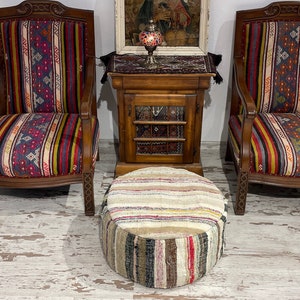 Può includere: Due poltrone in legno con rivestimento a strisce colorate e un pouf rotondo intrecciato multicolore davanti a un mobile in legno con una porta chiusa.