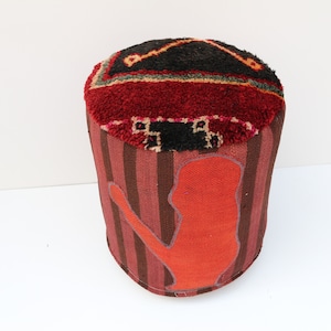 Pode incluir: Um pufe com padrão vermelho, marrom e preto com uma silhueta de uma pessoa no lado.