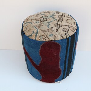 May include: A round, blue and red patterned ottoman with a beige top. The top is covered in a floral patterned fabric.