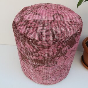 May include: Pink and brown patterned fabric ottoman. The ottoman is round and has a smooth surface.