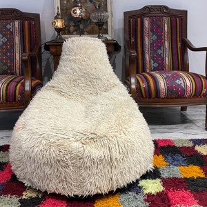 Peut inclure: Un fauteuil poire blanc et moelleux se trouve devant deux fauteuils en bois avec un revêtement à motifs colorés. Les fauteuils sont dans une pièce avec un tapis à motifs au sol.