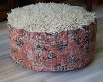 Könnte beinhalten: Ein runder, cremefarbener, flauschiger Hocker mit einem roten, blauen und cremefarbenen Muster an der Basis.
