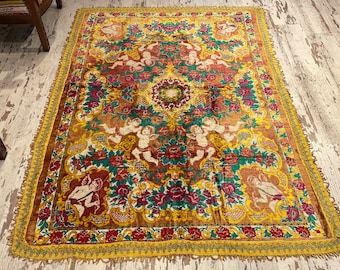 Puede incluir: Una alfombra vintage con un diseño floral y de querubines colorido. La alfombra tiene un borde dorado y flecos.