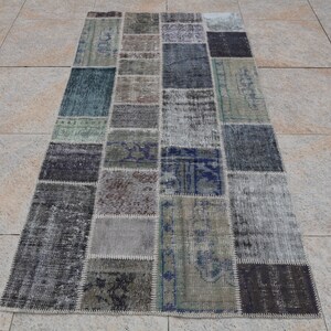 May include: A rectangular patchwork rug with a variety of colors and patterns. The rug is made up of smaller squares and rectangles of different fabrics, including denim, cotton, and wool. The rug has a distressed look, with faded colors and worn edges.