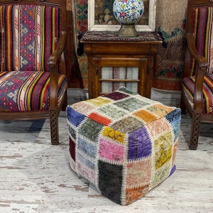 Może przedstawiać: Kolorowy otoman w stylu patchwork o kwadratowym kształcie, stojący przed dwoma krzesłami z wzorzystą tapicerką. Krzesła i otoman znajdują się w pokoju z drewniana podłogą i drewnianym stolikiem.