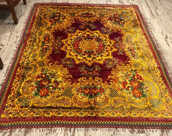 Puede incluir: Una alfombra roja, amarilla y verde con un diseño floral. La alfombra tiene un borde de flecos.
