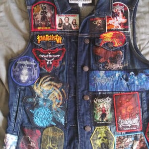 Puede incluir: Un chaleco vaquero con múltiples parches de bandas, incluyendo "Pantera" y "DevilDriver". El chaleco tiene una parte delantera abotonada y un cuello clásico. Los parches presentan varios colores y diseños, mostrando un tema de heavy metal.