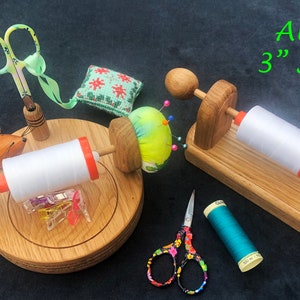 Può includere: Accessori per cucito, tra cui porta rocchetti in legno con filo bianco, un cuscinetto per spilli, forbici e un piccolo topo di legno. L'immagine include anche il testo "Aurifil 3" Spools".