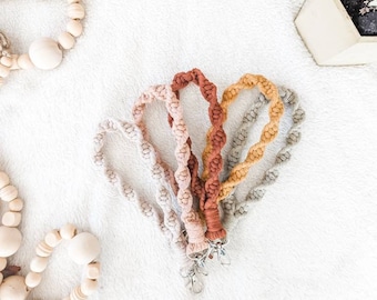 May include: Four colourful braided keychains with metal clasps. The keychains are in shades of beige, light brown, orange, and grey.