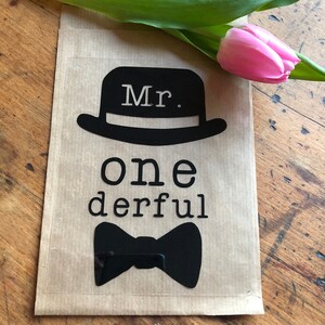 Könnte beinhalten: Eine braune Papierkarte mit einer schwarzen Silhouette eines Zylinders mit dem Wort "Mr." darin. Unter dem Hut steht der Text "one derful" und eine schwarze Fliege.