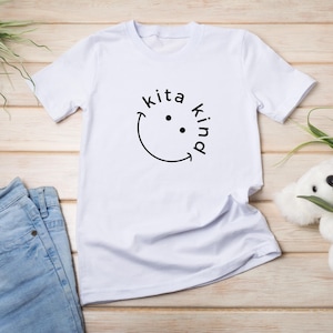 Könnte beinhalten: Weißes T-Shirt mit einem schwarzen Smiley und dem Text "Kita Kind" auf der Vorderseite.