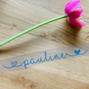Könnte beinhalten: Ein transparenter Vinyl-Aufkleber mit dem Namen "pauline" in blauer Kursivschrift mit einem Herz auf jeder Seite des Namens.