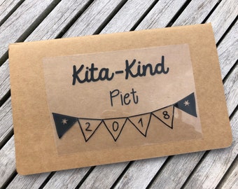 May include: A brown cardboard folder with a clear plastic sticker that says "Kita-Kind Piet 2018" with black stars and numbers on a banner.