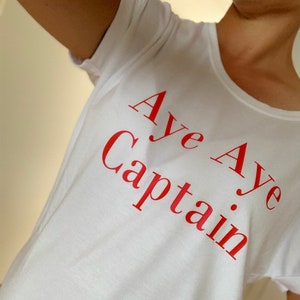 Könnte beinhalten: Weißes T-Shirt mit dem Aufdruck "Aye Aye Captain" in Rot.