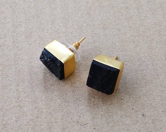 May include: A pair of gold-toned earrings with black square-shaped stones. The stones have a rough, textured surface.