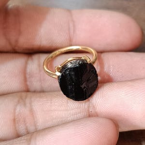 May include: A gold ring with a black oval shaped gemstone. The gemstone has a rough, natural texture.