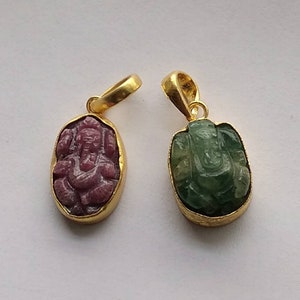 May include: Two gold pendants with carved Ganesha figures. One pendant features a pink stone and the other a green stone.