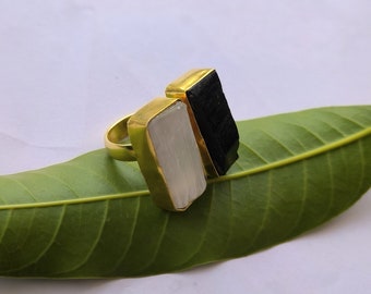 May include: Gold ring featuring a white and black stone setting. The ring is resting on a green leaf.