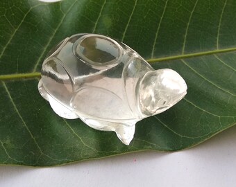 May include: A clear crystal turtle figurine with a smooth, polished finish. The turtle is sitting on a green leaf.