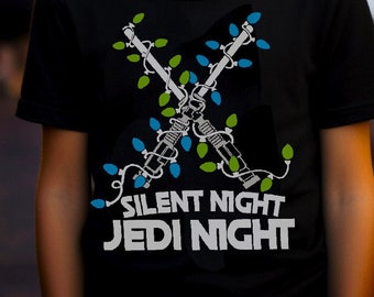 May include: A black t-shirt with a graphic of two crossed lightsabers made of Christmas lights. The text "Silent Night Jedi Night" is printed below the lightsabers.