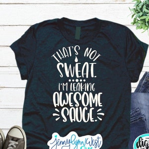 May include: A dark blue t-shirt with white text that reads "That's not sweat. I'm leaking awesome sauce." The shirt is on a white wooden background.