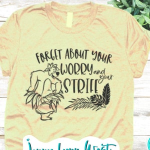 May include: A light yellow t-shirt with a black and white graphic of a cartoon bear with the text "Forget about your worry and your strife". The text "Jenny Lynn West SVG" is at the bottom of the shirt.