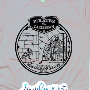 May include: A gray t-shirt with a black and white graphic of the Pirates of the Caribbean ride at Disneyland's New Orleans Square. The graphic includes the ride's name, the text "Disneyland" and "New Orleans Square", and the year "Est. 1967".