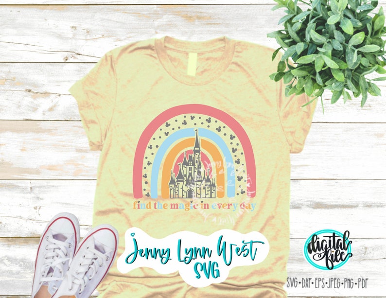 Op de afbeelding: Een lichtgeel T-shirt met een regenboog en een kasteel afbeelding. De tekst "find the magic in every day" is onder de afbeelding gedrukt. De tekst "Jenny Lynn West SVG" is onder de tekst gedrukt.