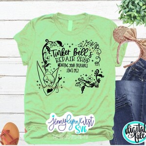 May include: A light green t-shirt with a black graphic design featuring Tinker Bell, a fairy, holding a wrench. The graphic includes the text "Tinker Bell's Repair Shop Mending Your Treasures Since 1953".