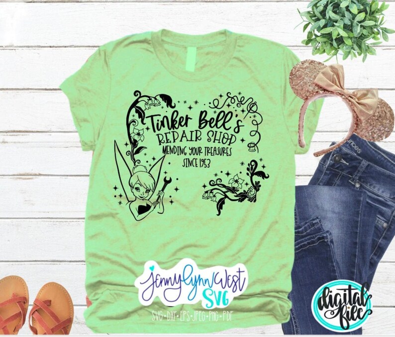 May include: A light green t-shirt with a black graphic design featuring Tinker Bell, a fairy, holding a wrench. The graphic includes the text "Tinker Bell's Repair Shop Mending Your Treasures Since 1953".