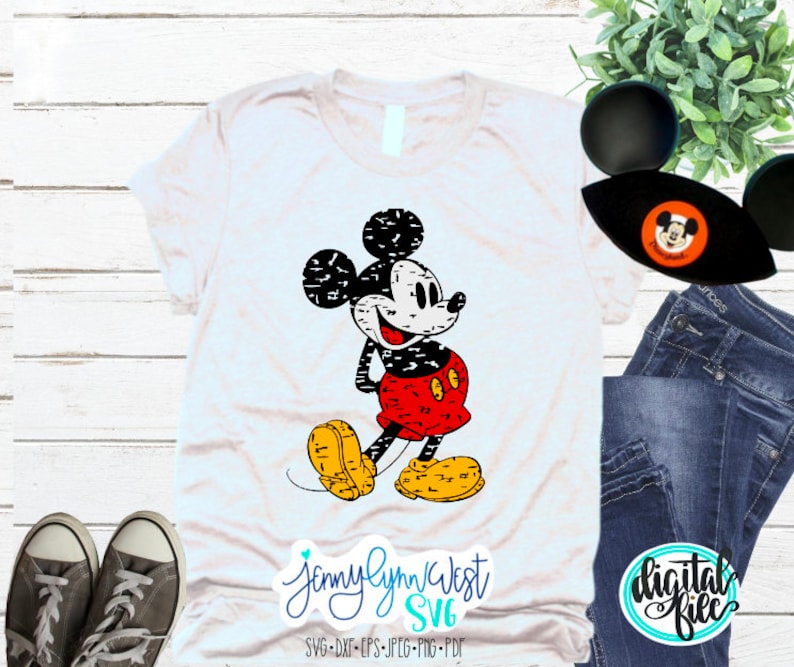 May include: A white t-shirt featuring a distressed black and white Mickey Mouse graphic. The graphic depicts Mickey Mouse wearing red and black shorts and a yellow smile. The text "Jennylynn West SVG" is printed in blue below the graphic.