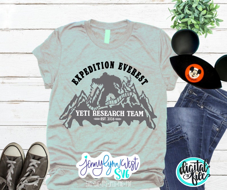 Pu&ograve; includere: Una maglietta grigia con un design grafico nero di uno Yeti in piedi di fronte a una catena montuosa. La grafica include il testo "EXPEDITION EVEREST", "YETI RESEARCH TEAM" e "EST. 2006".