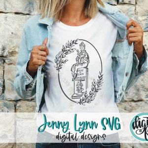 May include: A white t-shirt with a black and white design of a tombstone with a woman sitting on top. The tombstone reads "Rest in Peace Our Beloved George". The design is surrounded by a wreath of leaves.