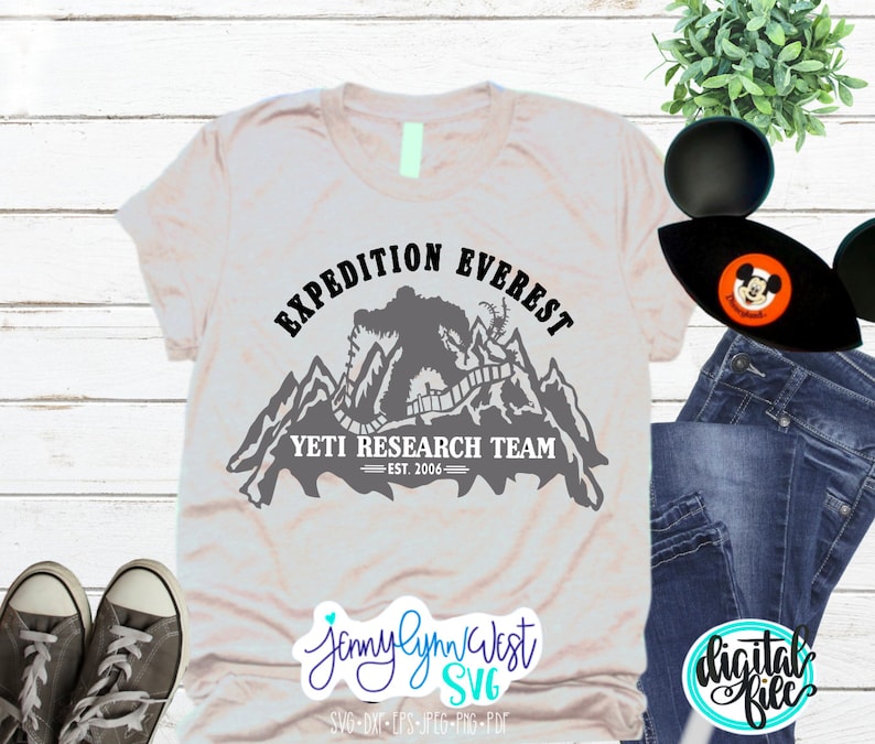 Pu&ograve; includere: Una maglietta grigia con un design grafico nero di uno Yeti in piedi su una catena montuosa. La grafica include il testo "Expedition Everest Yeti Research Team Est. 2006".