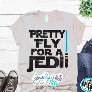 May include: A light beige t-shirt with black text that reads "PRETTY FLY FOR A JEDI" with a blue lightsaber graphic. The text "Jennylynn West SVG" is in pink and black at the bottom of the shirt.