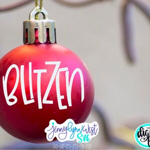 May include: A red Christmas ornament with the word "Blitzen" written in white on it. The ornament is hanging from a branch.