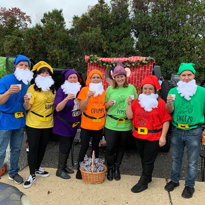 May include: Seven people dressed as the seven dwarfs from Snow White. They are wearing colourful shirts with their dwarf names on them. They are holding small cups and smiling.