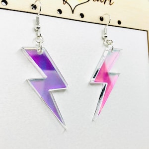 May include: A pair of iridescent lightning bolt earrings with silver hooks. The earrings are made of clear acrylic with a holographic finish.
