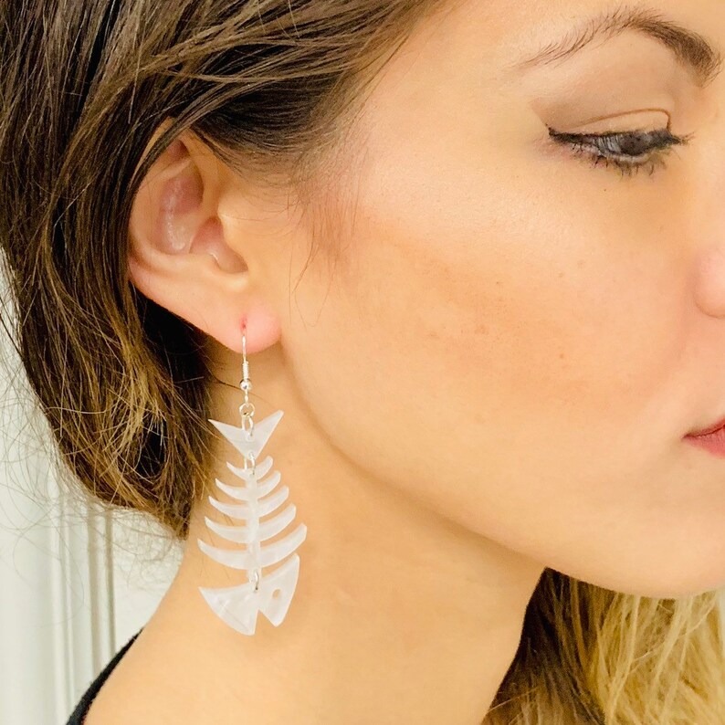 May include: White fish bone shaped earrings. The earrings are made of a translucent white material and have a silver hook.